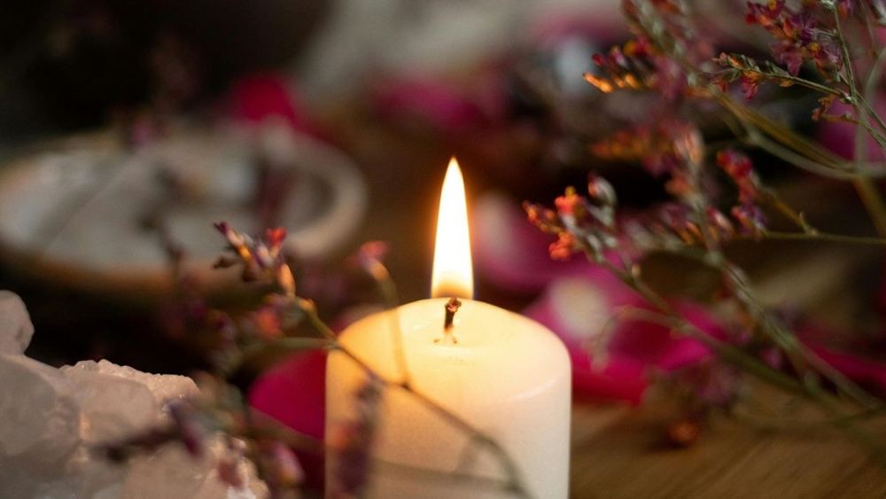 A white candle burning softly among dried flowers