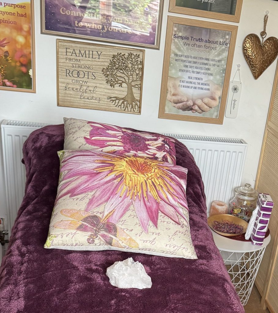 My treatment couch in the healing room, with a purple throw, cushions and a clear quartz crystal.